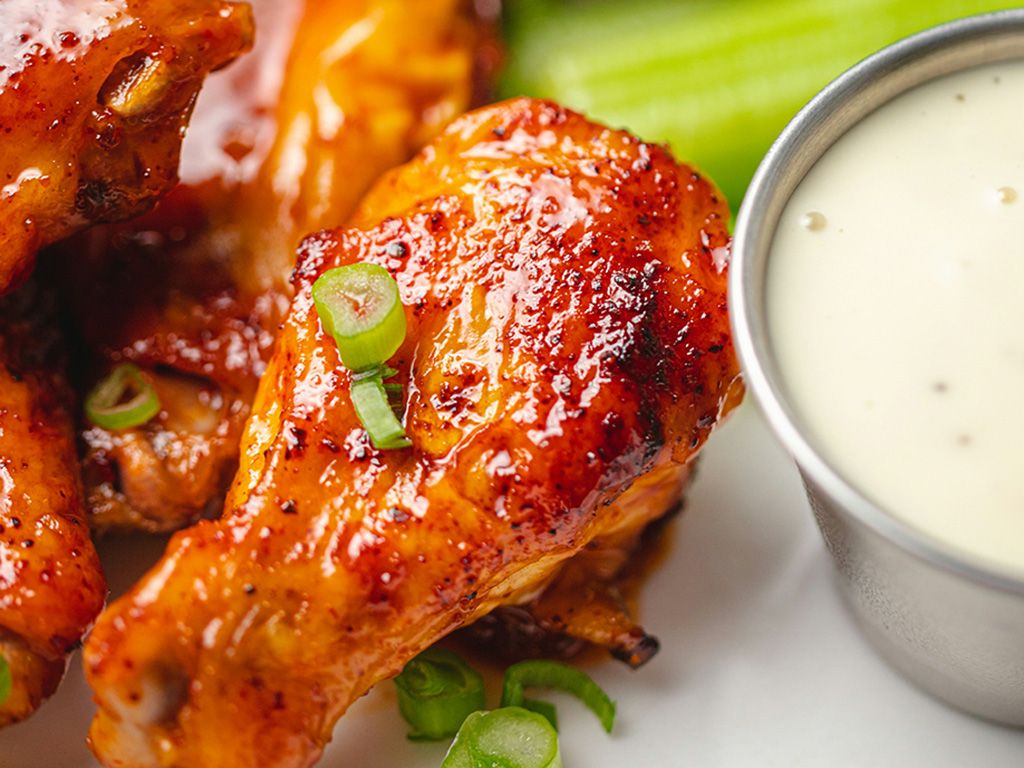 Chicken wings covered in hot sauce and green onions next to a small container of ranch dressing.