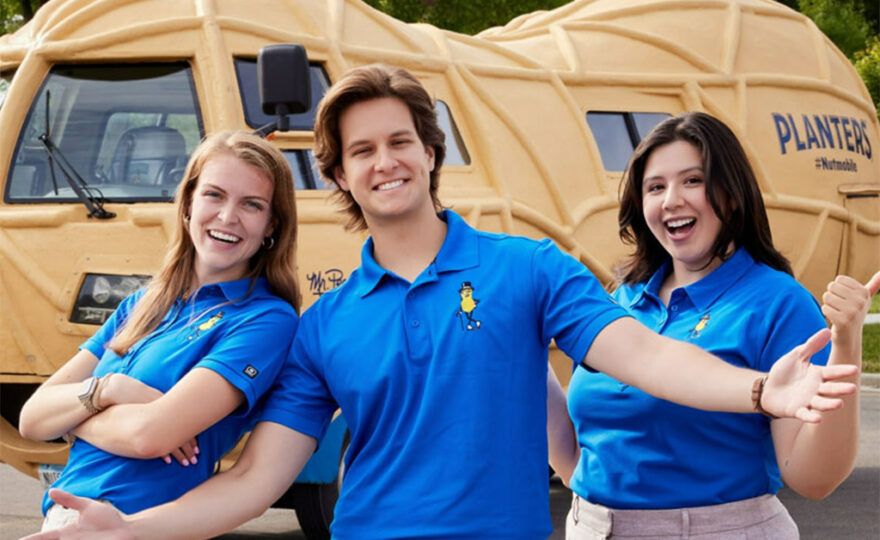 Three people in blue shirts standing in front of the Planters peanut mobile