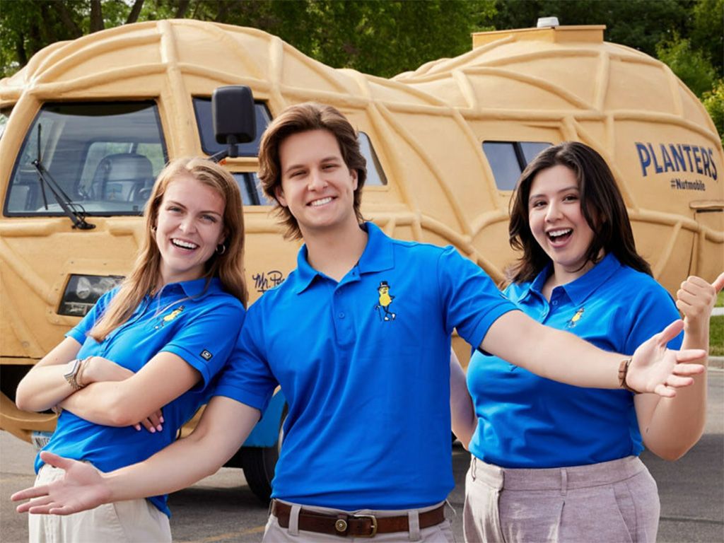 Three people in blue shirts standing in front of the Planters peanut mobile