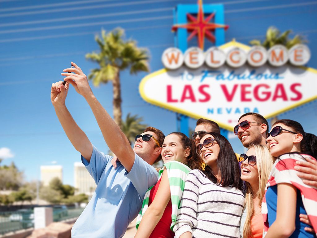 travel and tourism concept - group of happy friends taking selfie by cell phone over welcome to fabulous las vegas sign background