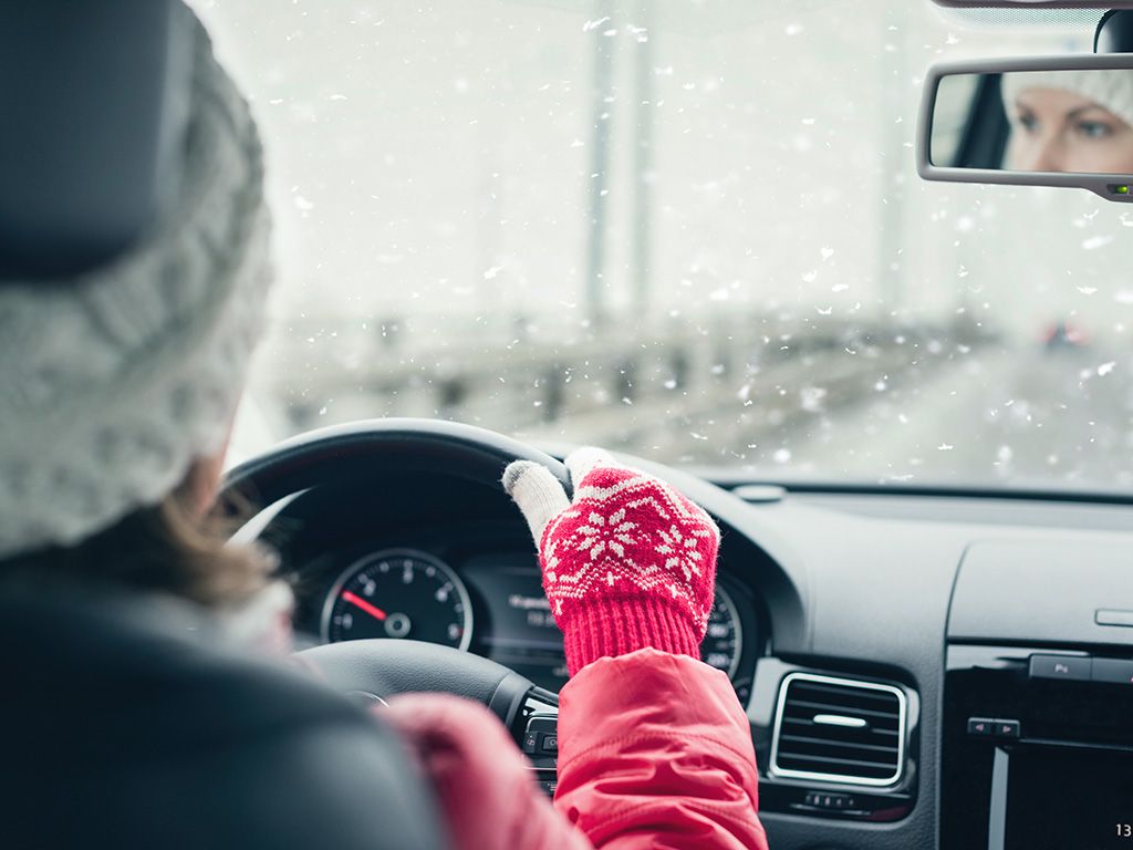 Woman driving in snow while wearing gloves and a hat