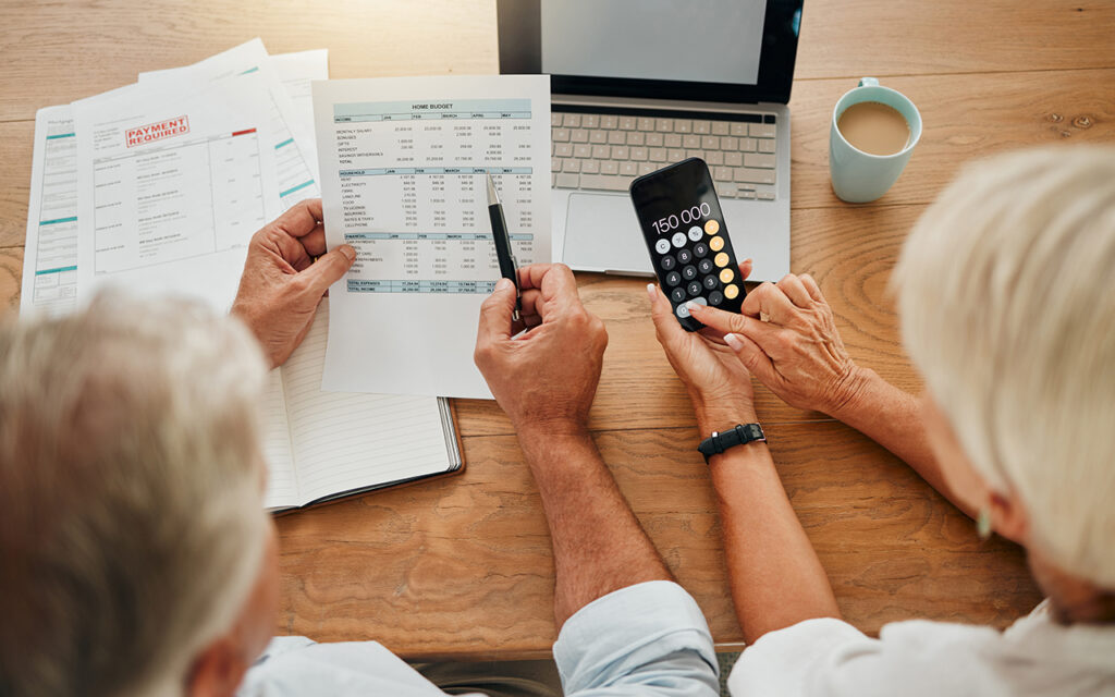 Elderly couple looking at paperwork, phone and laptop