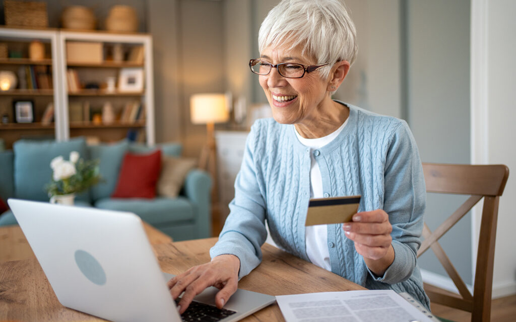 Happy senior woman using laptop and credit card for online shopping at home